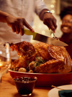 Close-up of black man carving roasted turkey during Thanksgiving meal at dining table.