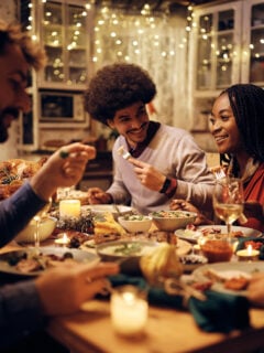 Group of happy friends eating at dining table while celebrating Thanksgiving and Friendsgiving together.