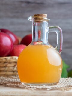 A bottle of raw unfiltered apple cider vinegar with fresh apples