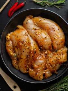 Raw chicken marinating in a bowl with seasoning around it