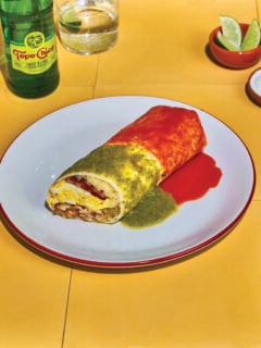 Photo of a New Mexico style breakfast burrito covered in red and green salsa on a white plate.