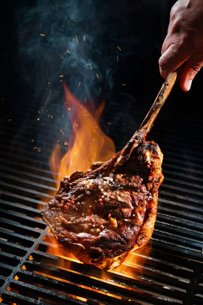 A Tomahawk steak being grilled over fire and being held by the long bone