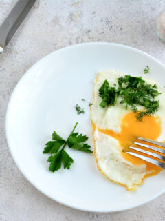 fried egg isolated on white plate with parsley, fork and knife, close-up
