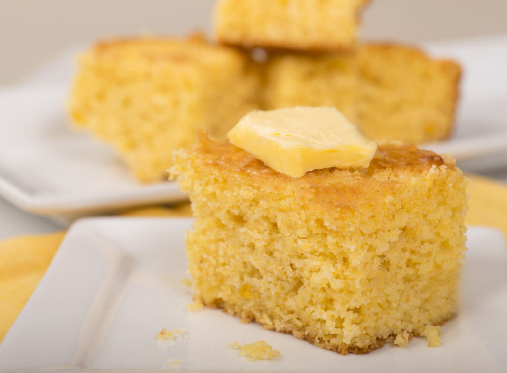 Piece of freshly baked cornbread with creamy butter on top.