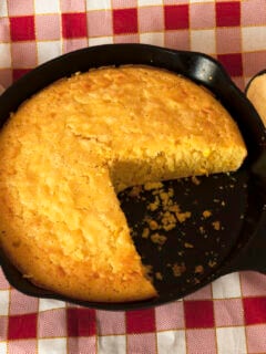 Homemade cornbread in a cast iron skilet, with eggs and a container of corn flour arranged on the side.