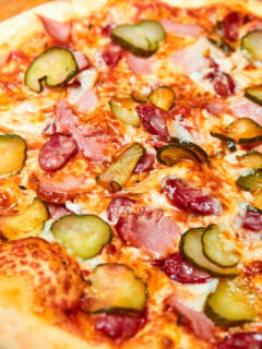 Fresh pizza pickles, bacon, sausages and cheese on a wooden board. Close-up, selective focus