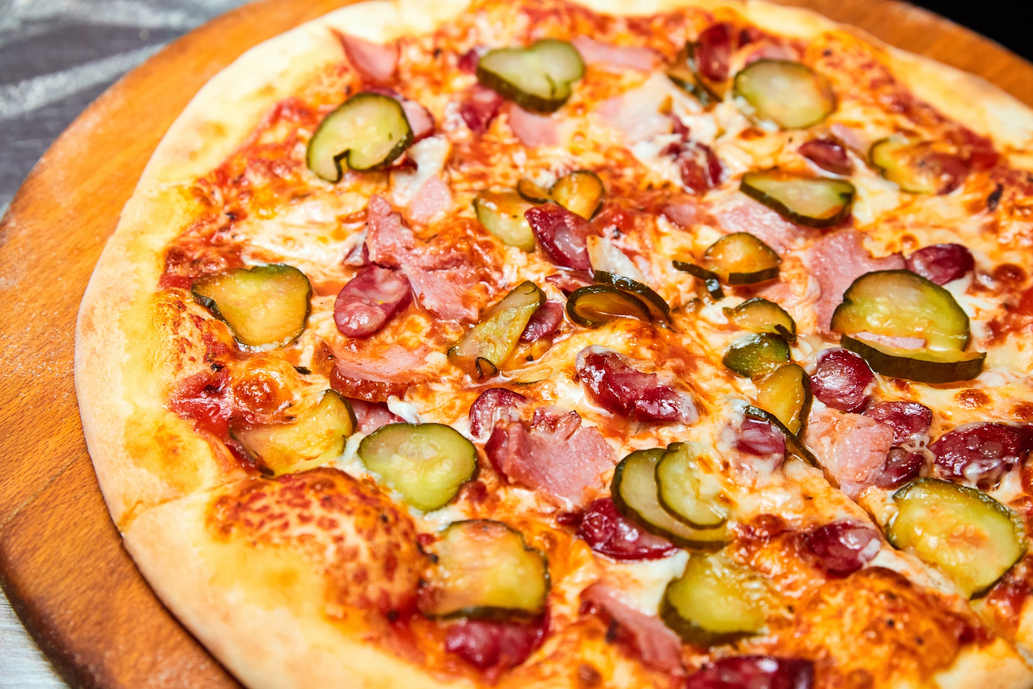 Fresh pizza pickles, bacon, sausages and cheese on a wooden board. Close-up, selective focus