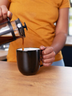A close up of a young woman pouring French press coffee into a mug in the kitchen. High quality photo