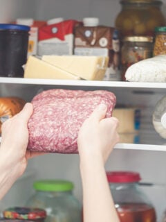Someone putting sealed ground beef in the refrigerator with two hands.