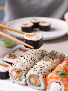 Woman taking tasty sushi roll with salmon from set at table, closeup