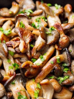 Fried mushrooms with fresh herbs in black cast iron pan.