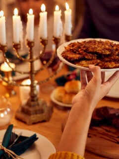 Close-up of couple passing latkes during a meal at dining table while celebrating Hanukkah at home.