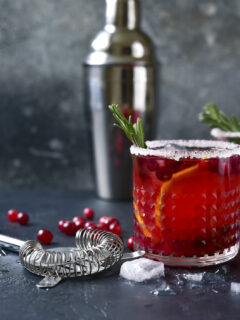 Red christmas cocktail with cranberries and oranges in a glasses on a dark slate, stone or concrete background
