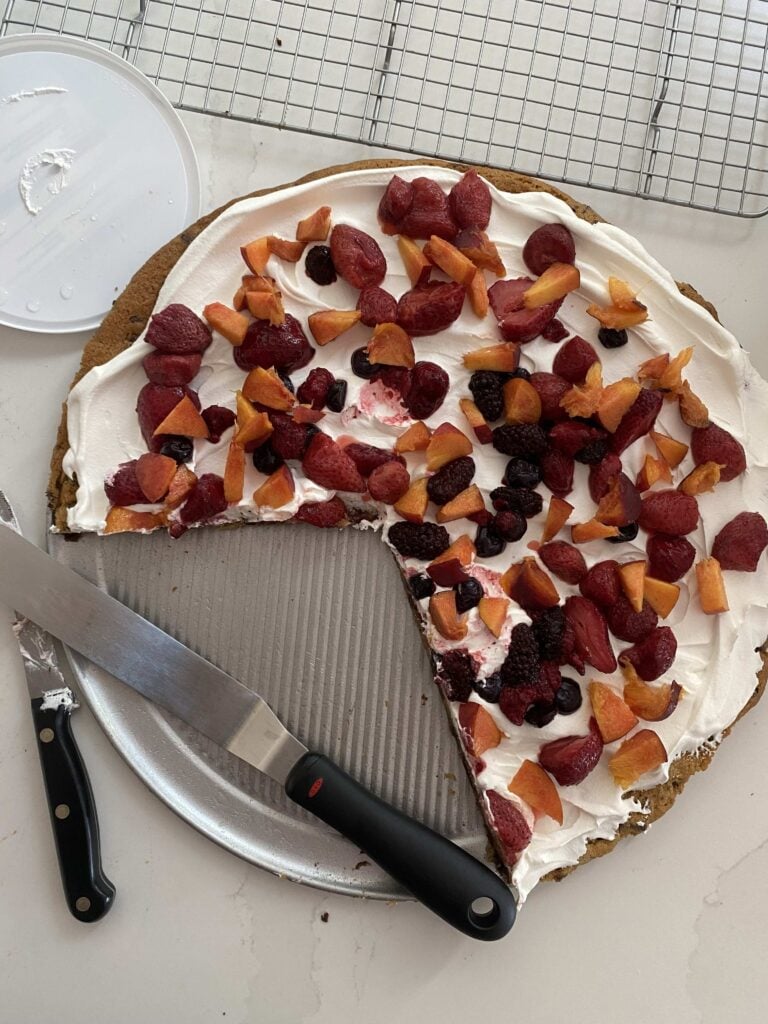 Cookie pizza topped with fruit, partially eaten.