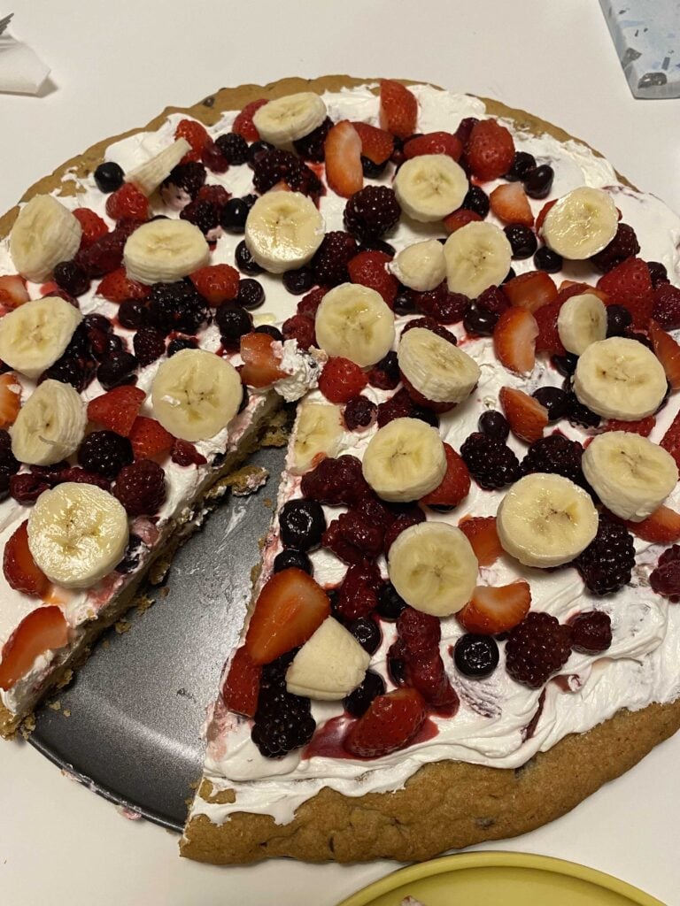 Our editor's cookie pizza, topped with bananas, strawberries, raspberries, and blueberries. One piece is missing.