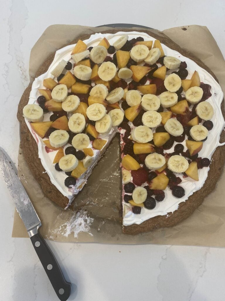 Cookie pizza seen from above, with one piece missing and a knife nearby.
