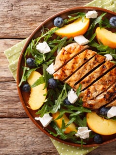Grilled chicken cutlet with fresh peaches, blueberries, arugula and feta cheese close-up on a plate on a table.