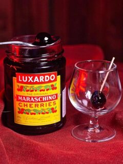 Jar of Luxardo maraschino cherries on a red cloth next to a cocktail glass.
