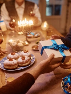 Close up of Jewish father giving his daughter gift box while celebrating Hanukkah with their family at home.