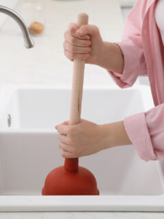 Woman using plunger to unclog sink drain in kitchen