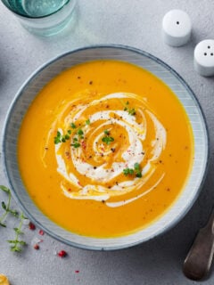 Pumpkin and carrot soup with cream on grey stone background.