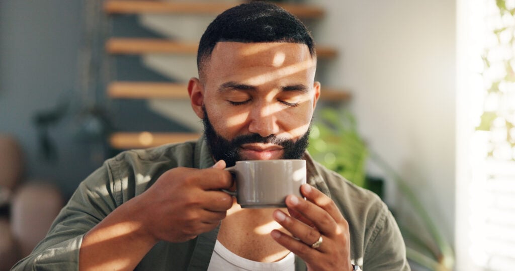 Calm man with drink by window in apartment