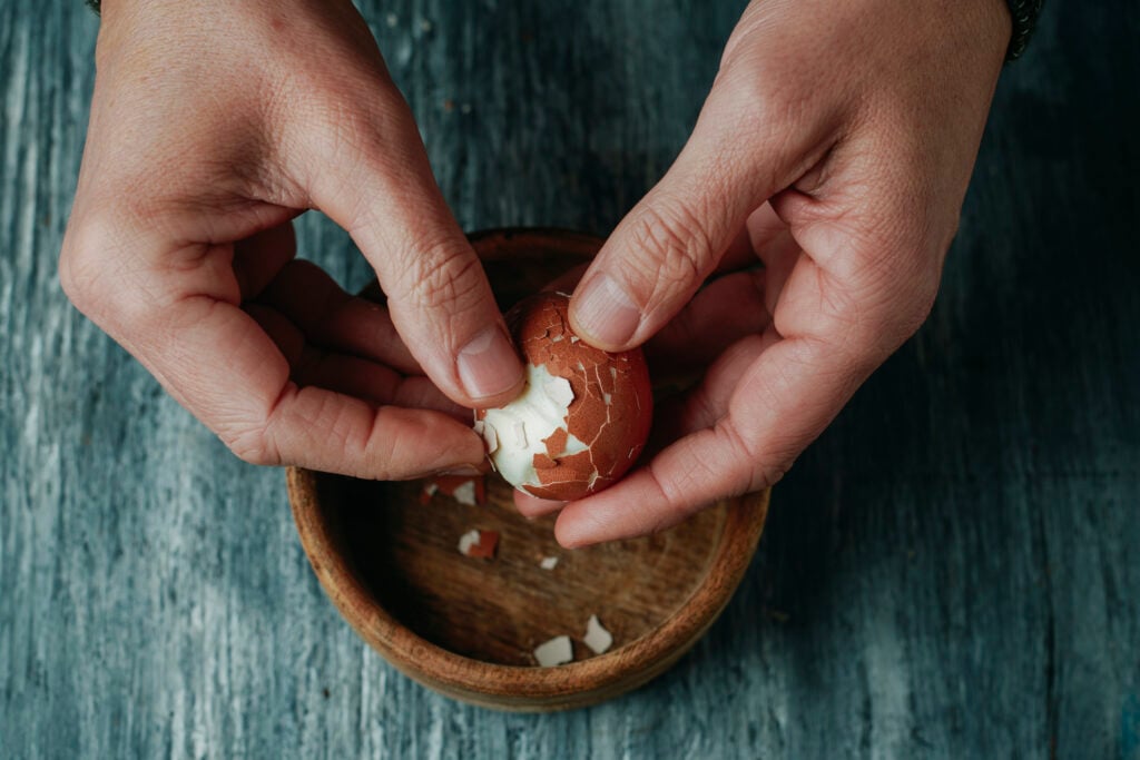 high angle view of a man peeling a hard-boiled egg at a rustic gray wooden table