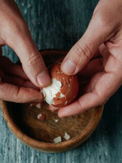 high angle view of a man peeling a hard-boiled egg at a rustic gray wooden table