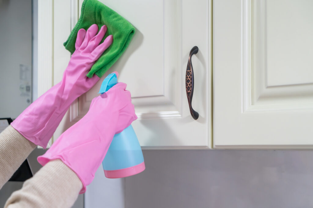 Spraying a kitchen cabinet to clean it and wearing gloves