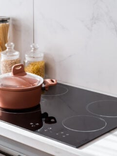 Clean new and black induction stove with control panel near marble countertop on white kitchen. Metal saucepan and jars with products on cooking surface. Cookery and homemade food concept