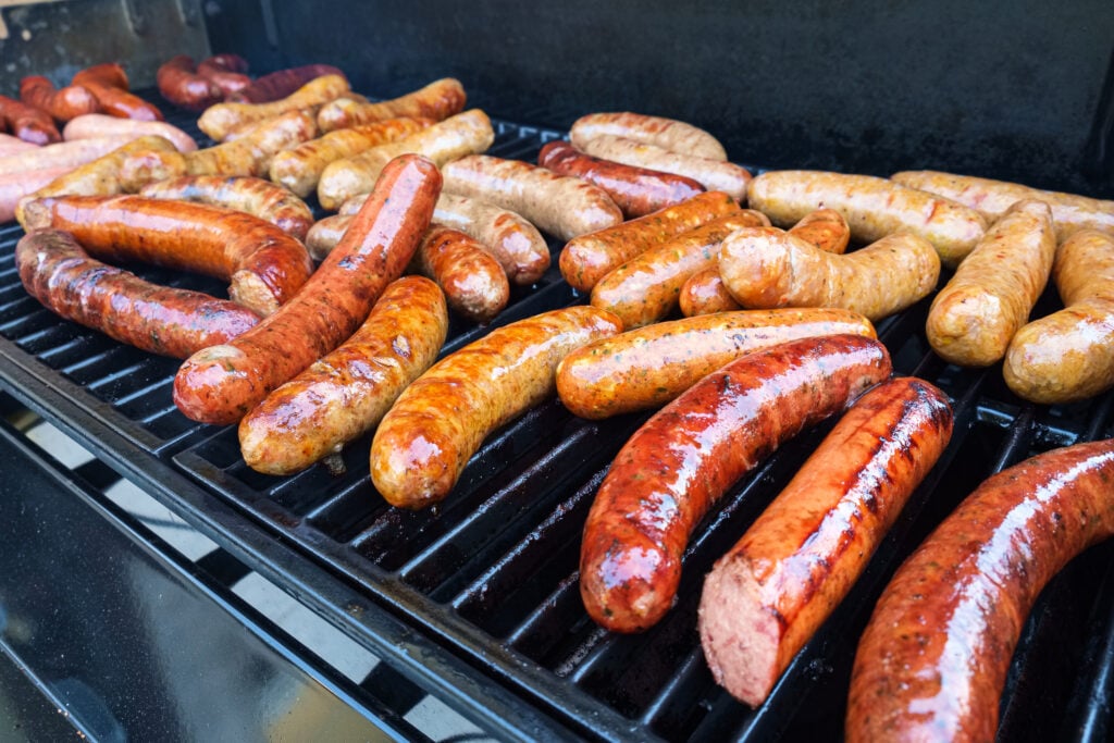 Fresh sausage and hot dogs grilling outdoors on a gas barbecue grill.