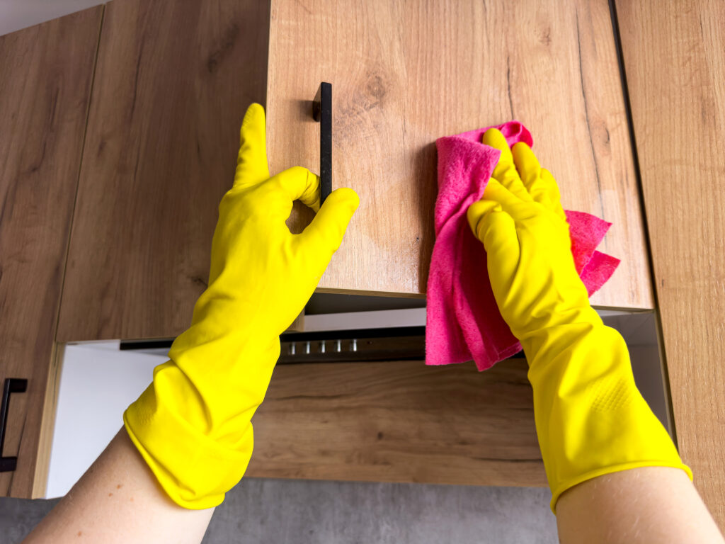 close up in yellow glove washing wooden cabinet in the kitchen.