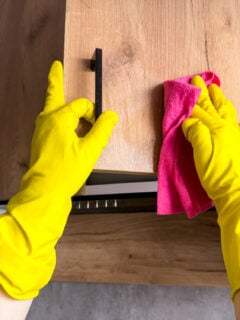 close up in yellow glove washing wooden cabinet in the kitchen.