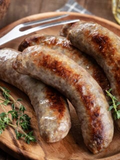 Fried bratwurst garnished with thyme on a plate on a rustic wooden table