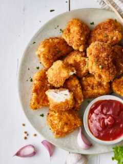 Chicken nuggets in a plate, with ketchup, salad and lemon, served on a white wooden restaurant or home table, top view with copy space