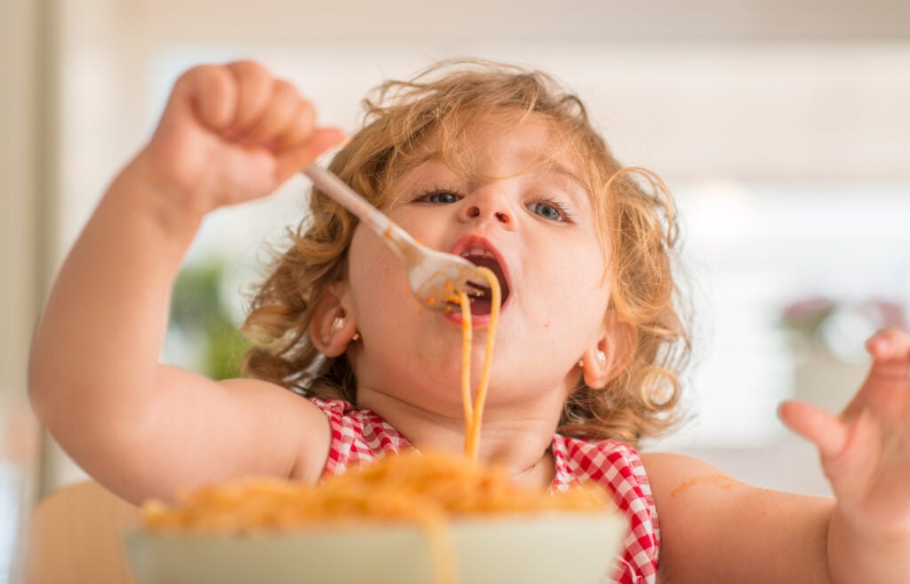 child eating spaghetti with fork at home