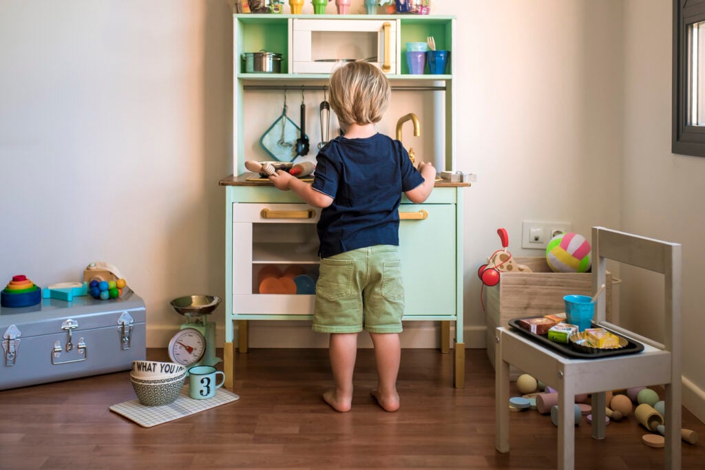 Little blond boy plays with a toy kitchen at home.
