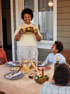 Portrait of senior black woman bringing food to table while enjoying family gathering outdoors