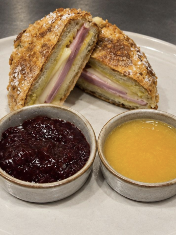 A Monte Cristo sandwich cut in half on a white plate with two dipping sauces.