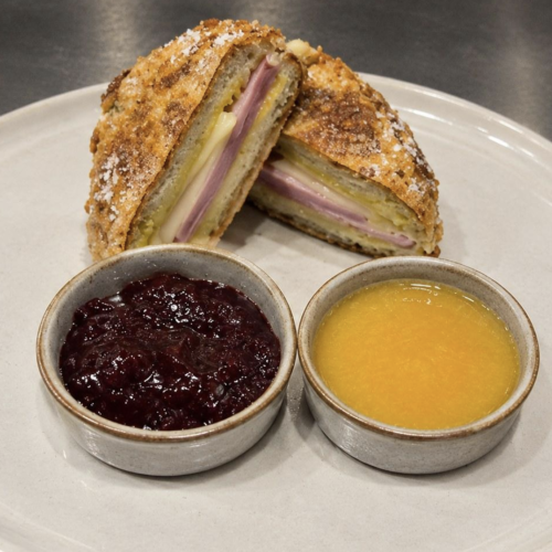 A Monte Cristo sandwich cut in half on a white plate with two dipping sauces.